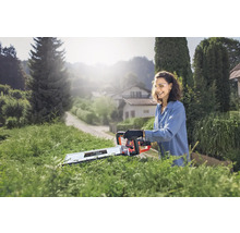 Vrouw snoeit heg met een accuheggenschaar in de tuin.