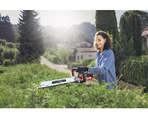 Vrouw snoeit heg met een accuheggenschaar in de tuin.