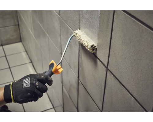 Een persoon schildert een betegelde muur met een verfroller.