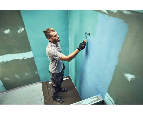 Man schildert een muur met een verfroller in een badkamer