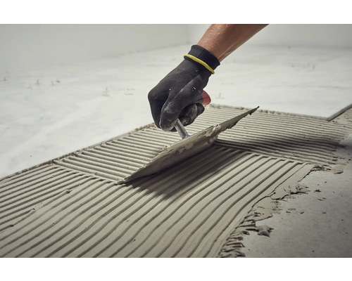 Tegelzetter brengt lijm aan op de vloer met een troffel