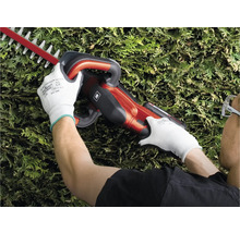 Een persoon snoeit een haag met een heggenschaar.