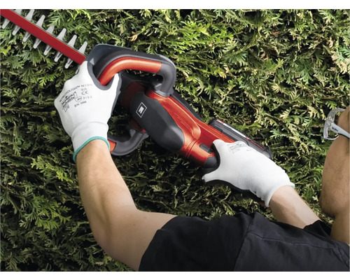 Een persoon snoeit een haag met een heggenschaar.