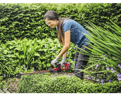 Een vrouw gebruikt een draadloze heggenschaar in de tuin om een haag te snoeien.