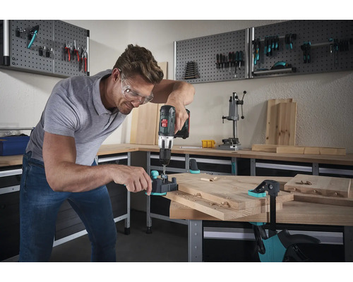 Man boort met een boormachine deuvelgaten in een houten plank op een werkbank.