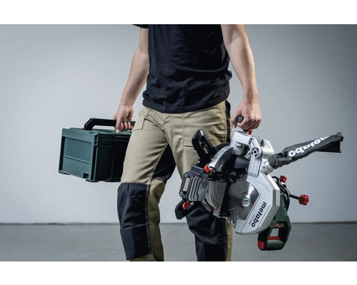 Een persoon draagt een Metabo verstekzaag en een gereedschapskoffer.