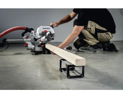 Een persoon bedient een Metabo verstekzaag om een stuk hout te zagen dat op een werkstuksteun rust.