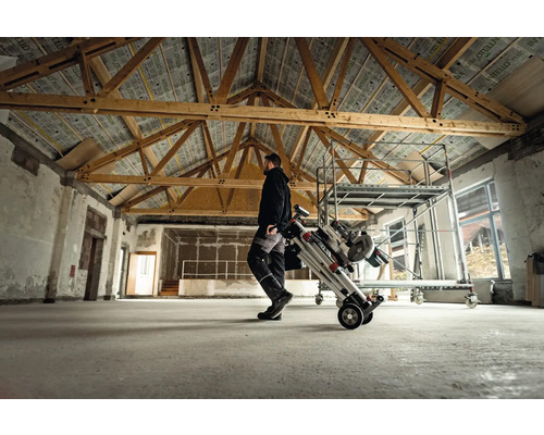 Man transporteert een rolsteiger in een ruimte met houten balken.
