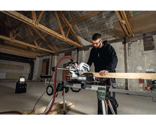 Man werkt met een Metabo verstekzaag in een ruwbouw om een houten plank te zagen.