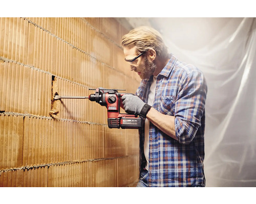Man boort met een boorhamer een gat in een bakstenen muur.