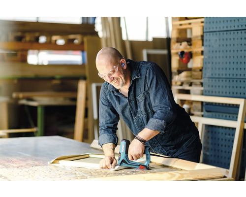 Een vakman bevestigt stof met een elektrische tacker aan een houten frame in een werkplaats.