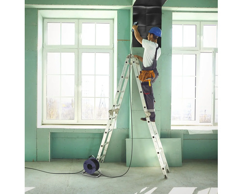 Vakman op een ladder bevestigt geluidsisolatieplaten aan een muur in een kamer.