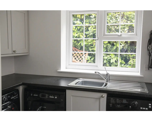 Lichte wasruimte met gootsteen, raam en wasmachine.