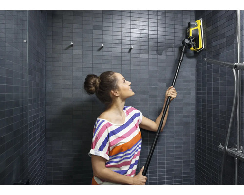 Vrouw reinigt een betegelde douche met een raamwisser met telescopische steel