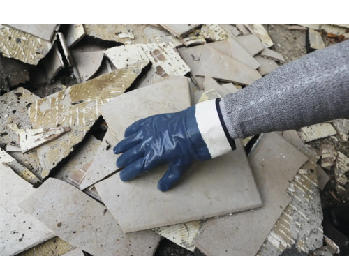 Een hand met beschermende handschoen op een hoop gebroken tegels