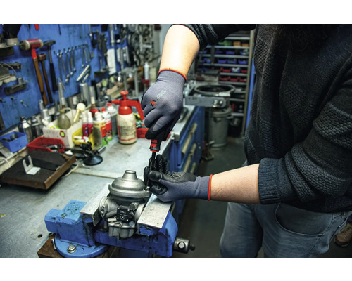 Een persoon werkt met een schroevendraaier en beschermende handschoenen aan een werkstuk dat in een bankschroef is bevestigd.