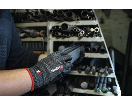 Een persoon draagt KinetiXx werkhandschoenen en haalt een stuk metaal uit een stelling met metalen buizen.