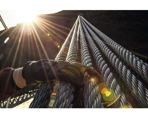 Hand met handschoen raakt stalen kabels aan