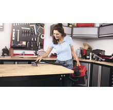 Een vrouw maakt een werkbank schoon met een nat- en droogzuiger in een werkplaats.