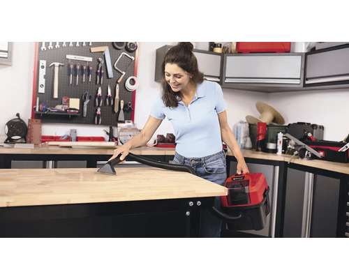 Een vrouw maakt een werkbank schoon met een nat- en droogzuiger in een werkplaats.