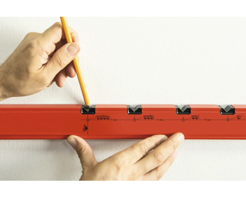 Hand markeert met potlood deuvelgaten op een muur met een boormal.