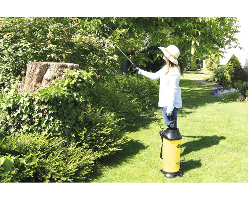 Tuinscene met vrouw die bomen behandelt met een plantenspuit