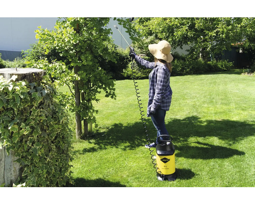 Vrouw gebruikt een gele drukspuit van Mesto in de tuin om een boom te behandelen.