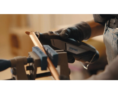 Een persoon gebruikt een Dremel 8240 multitool om een koperen buis te snijden die in een bankschroef is vastgeklemd.