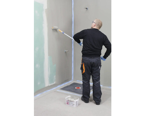 Ambachtsman bedekt een badkamermuur met een verfroller. Voorbereide badkamer met afdichting en doucheputje.