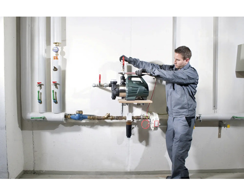 Installatie van een tuinpomp door een vakman op een muur met leidingen.