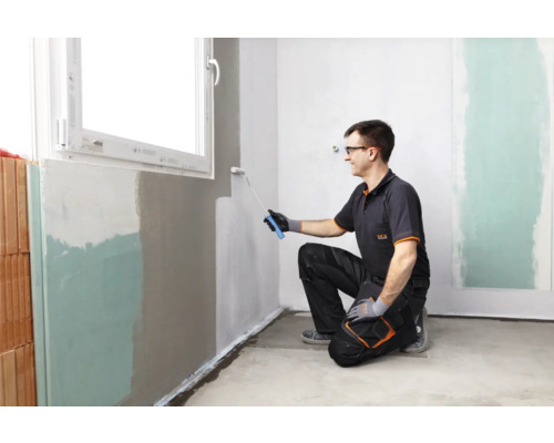 Een man verft een muur met een verfroller in een kamer.