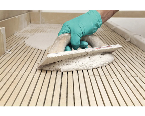 Een vakman brengt tegellijm aan op tegels met een spaan.