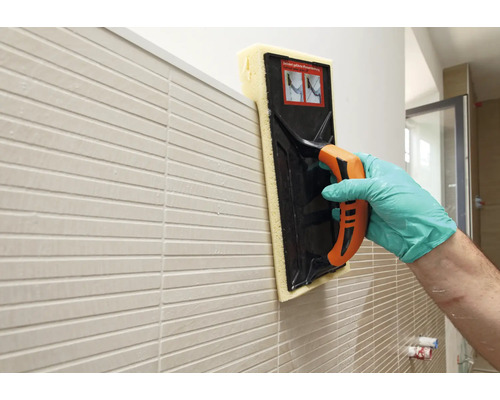 Tegelzetter maakt een muur schoon met een voegsponsbord.