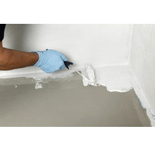 Een persoon verzegelt een vloerwandhoek met een verfroller en waterdichte coating.