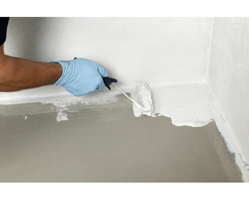 Een persoon verzegelt een vloerwandhoek met een verfroller en waterdichte coating.