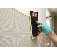 Tegelzetter reinigt een betegelde muur met een sponsbord.