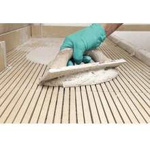 Een vakman met handschoenen voegt tegels met een voegspaan.