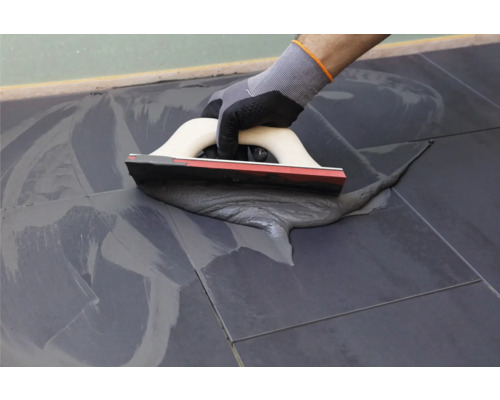 Tegelzetter met spatel bij het voegen van tegels