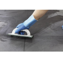 Iemand voegt grijze tegels met een voegbord.