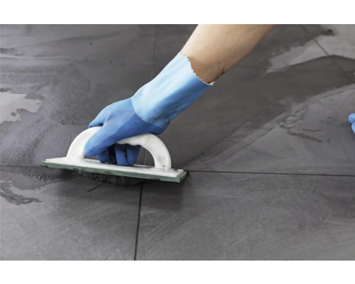 Iemand voegt grijze tegels met een voegbord.