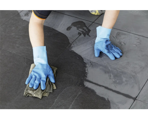 Een persoon reinigt vloertegels met een doek en handschoenen