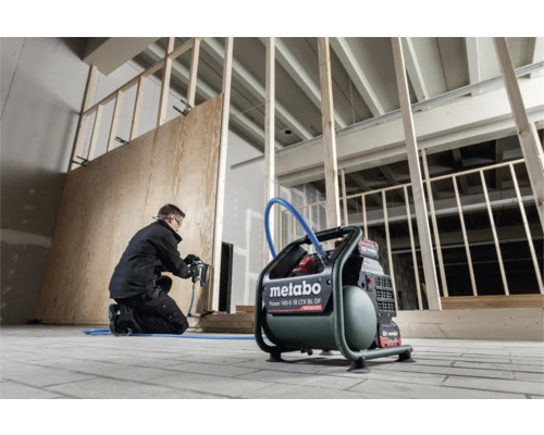 Ambachtsman bevestigt met een pneumatische tacker een houten plaat aan een muur, met een Metabo compressor op de voorgrond