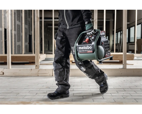 Een persoon draagt een Metabo Power 160-5 18 LTX BL OF compressor op een bouwplaats.