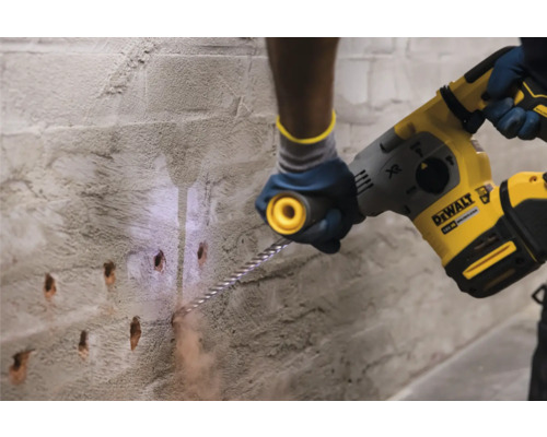 Iemand boort met een boorhamer gaten in een muur.