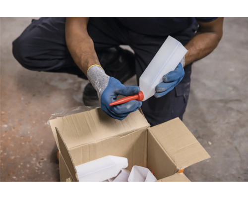 Iemand plaatst een rode tuit op een lege plastic fles boven een kartonnen doos.