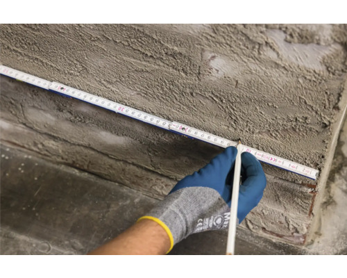 Hand met potlood markeert een meting op een duimstok op een muur