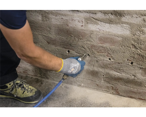 Man reinigt boorgaten in een muur met perslucht