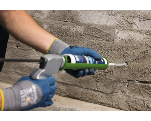 Persoon gebruikt een kitspuit op een muur om een voeg af te dichten.