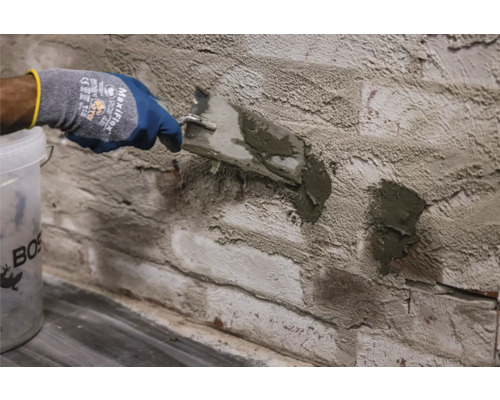 Vakman voegt een bakstenen muur met een plamuurmes en voegmortel