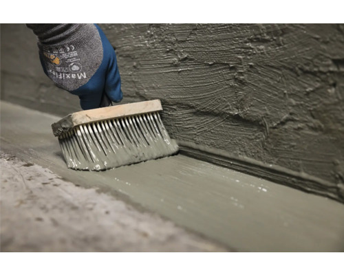 Iemand brengt met een kwast een afdichting aan op wand en vloer.